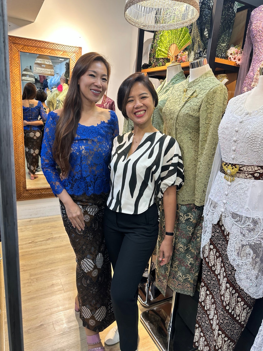 Two people posing in the Mozaic boutique beside kebaya displays