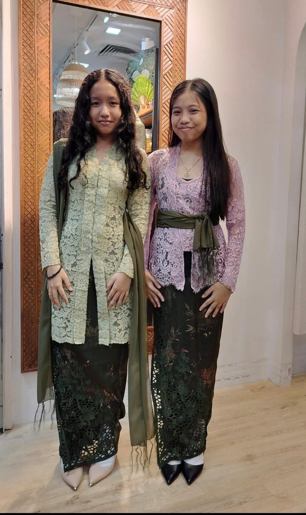 Two people wearing green and lilac kebayas with batik skirts in the boutique