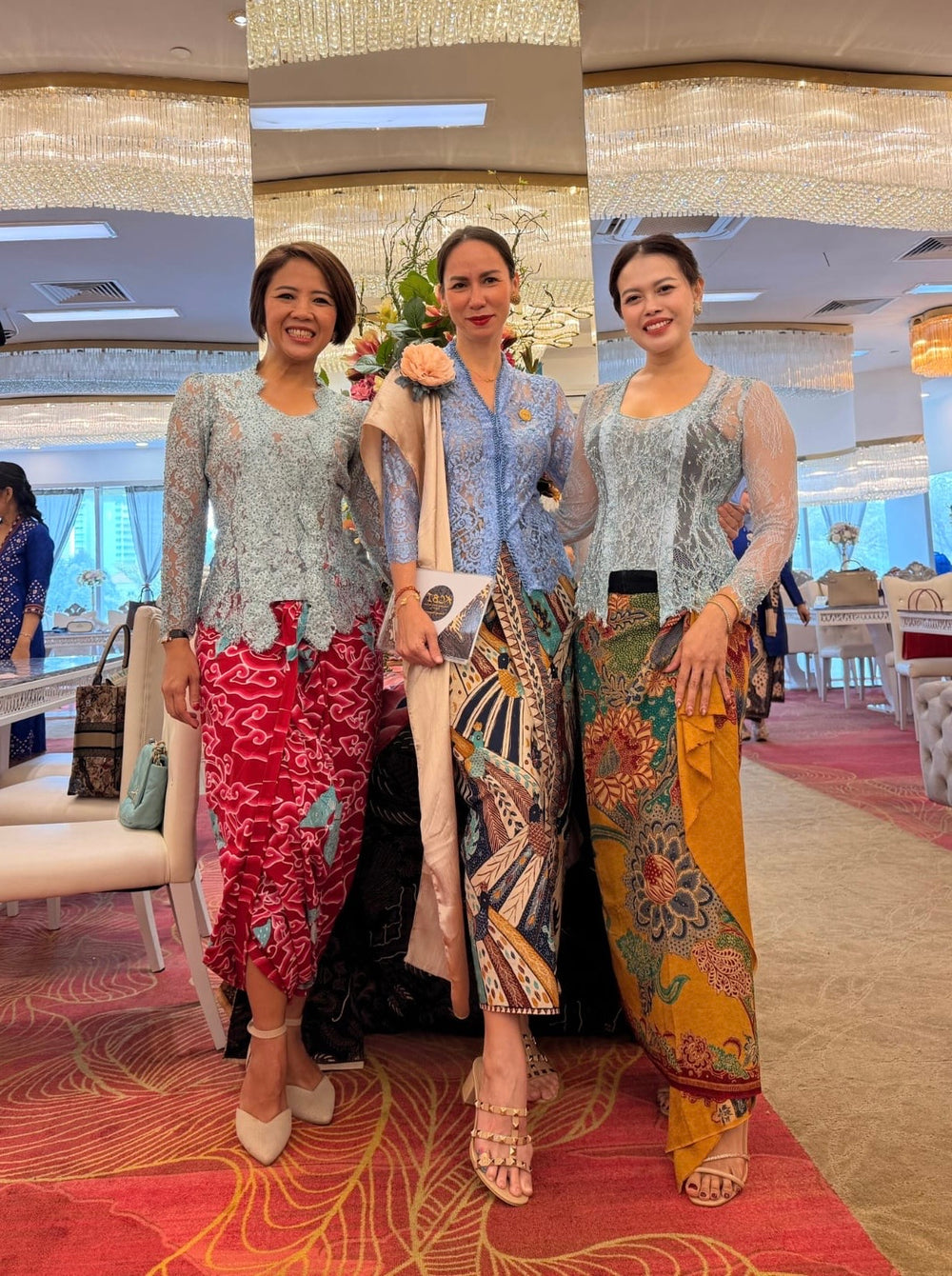 Three women wearing lace kebaya and patterned batik skirts at a celebration.